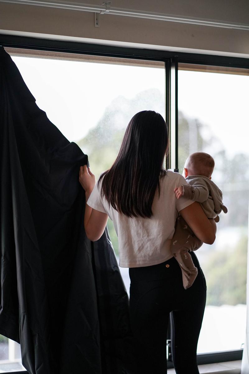 Mum holding baby while setting up My Blackout Blind on nursery window